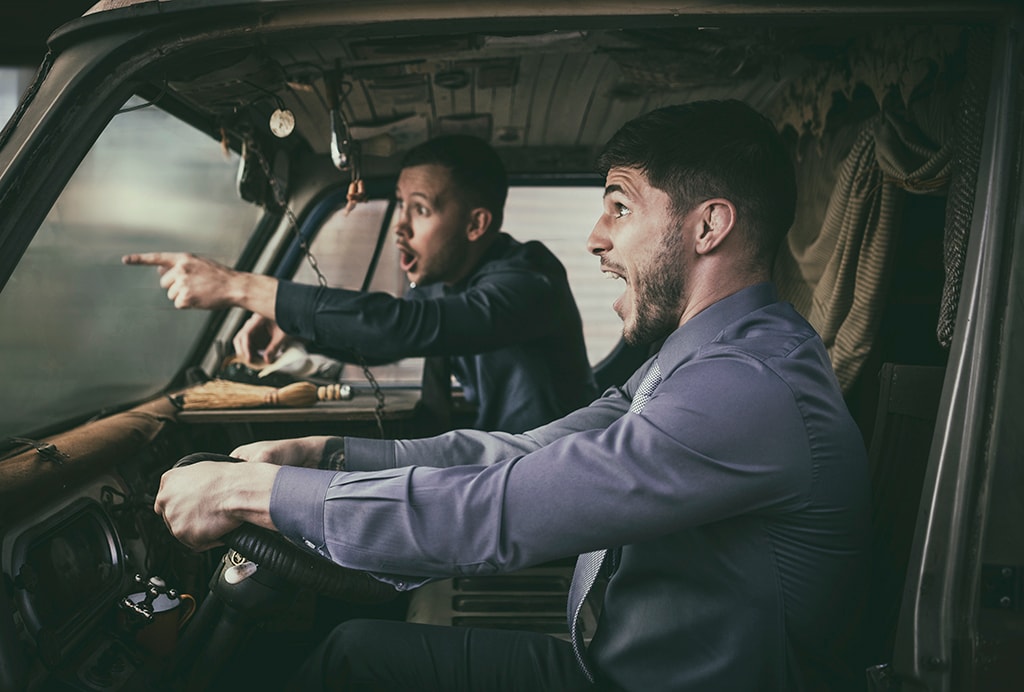 Two men in suits reacting dramatically inside vintage truck cab