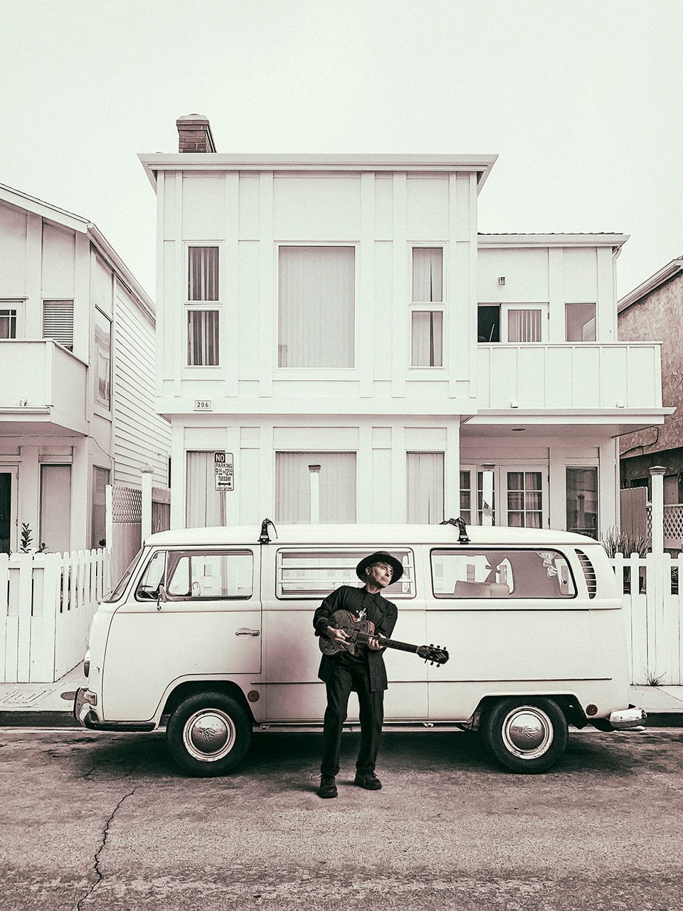 Musician with guitar standing before vintage VW van and beach house