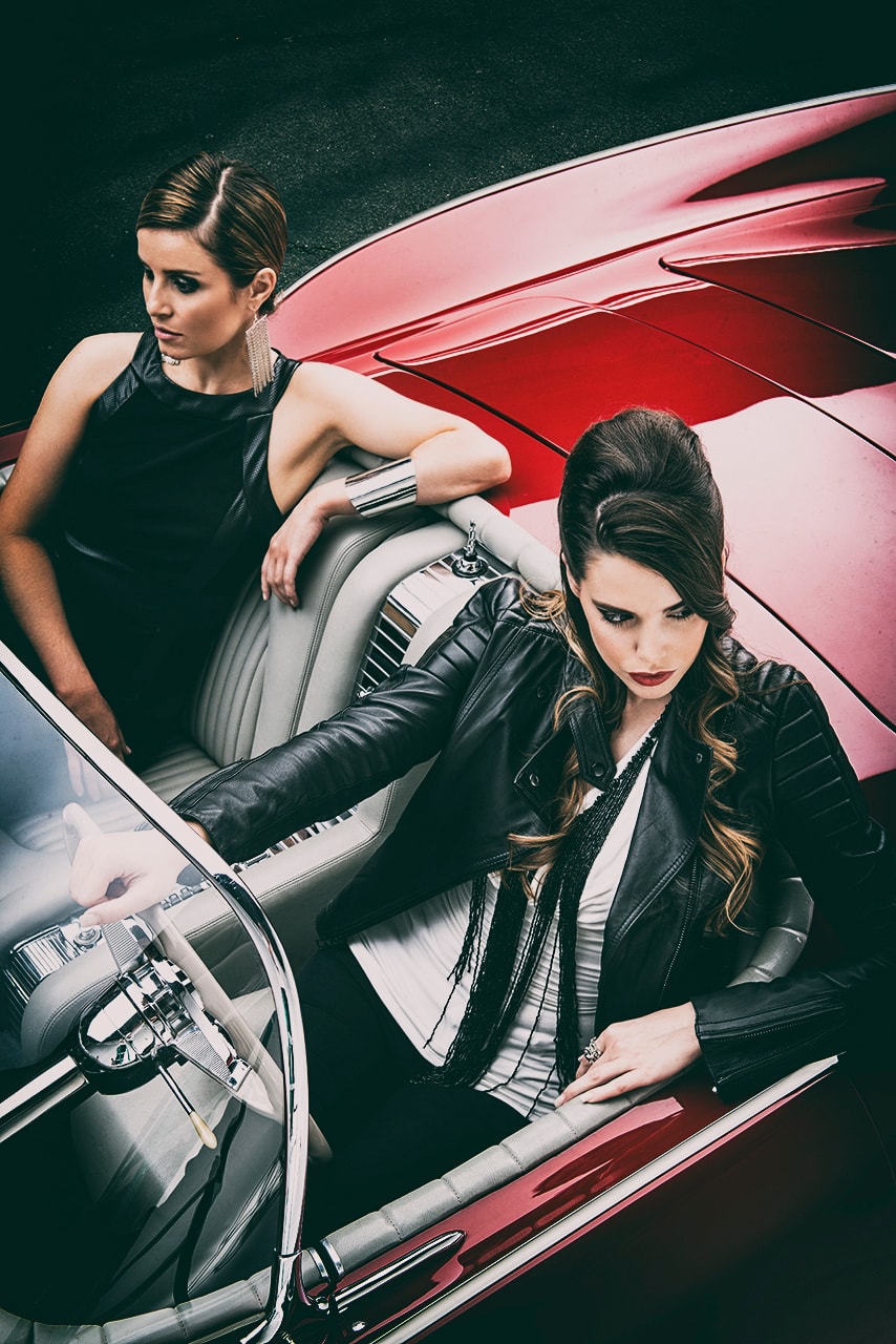 Two women in leather jackets posed in and around red vintage convertible