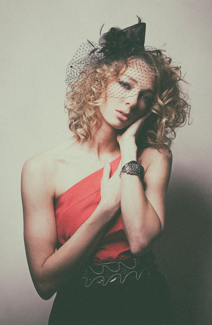 Woman in red dress and birdcage veil, moody studio fashion portrait