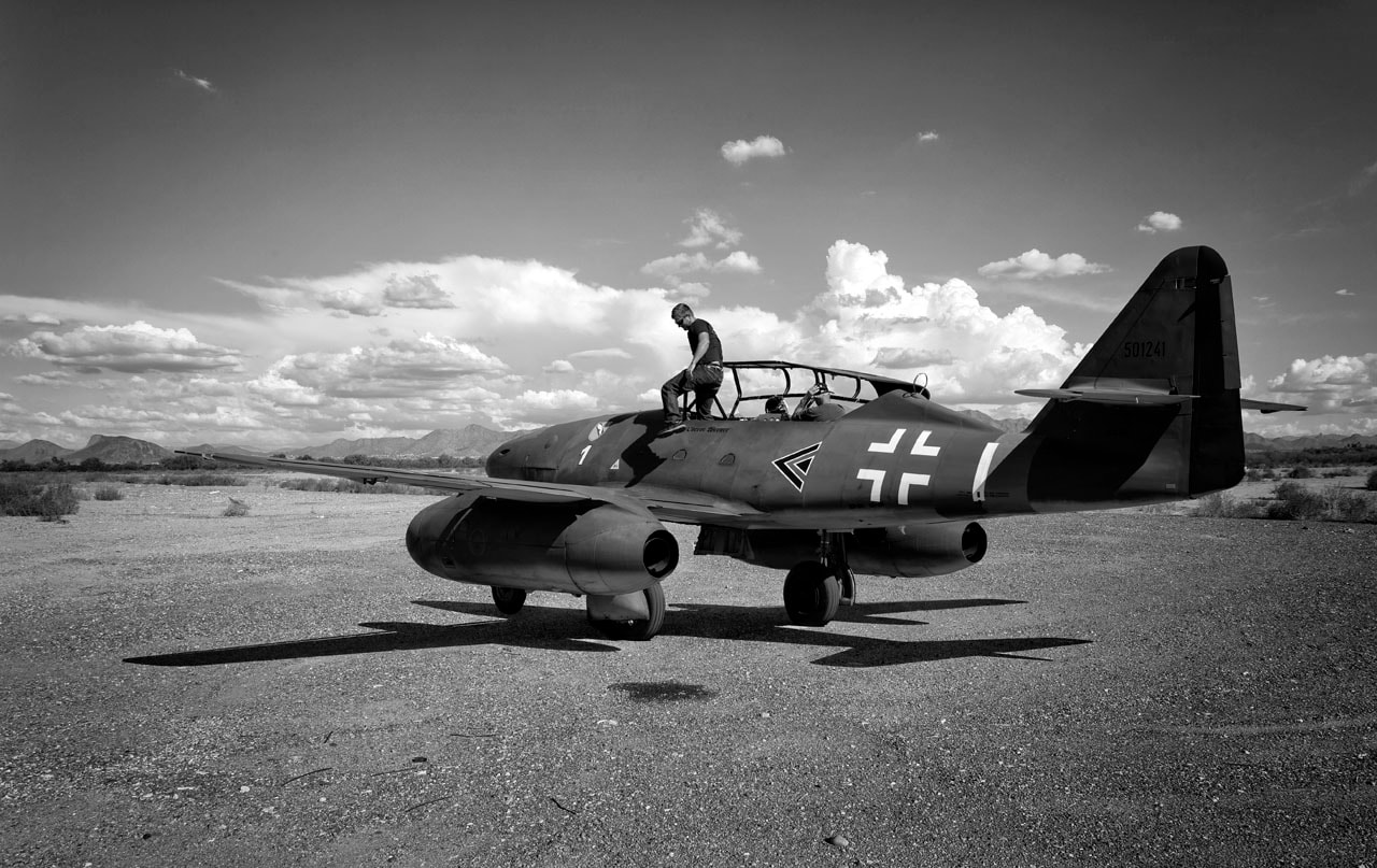 Man climbing into vintage WWII aircraft on desert airfield