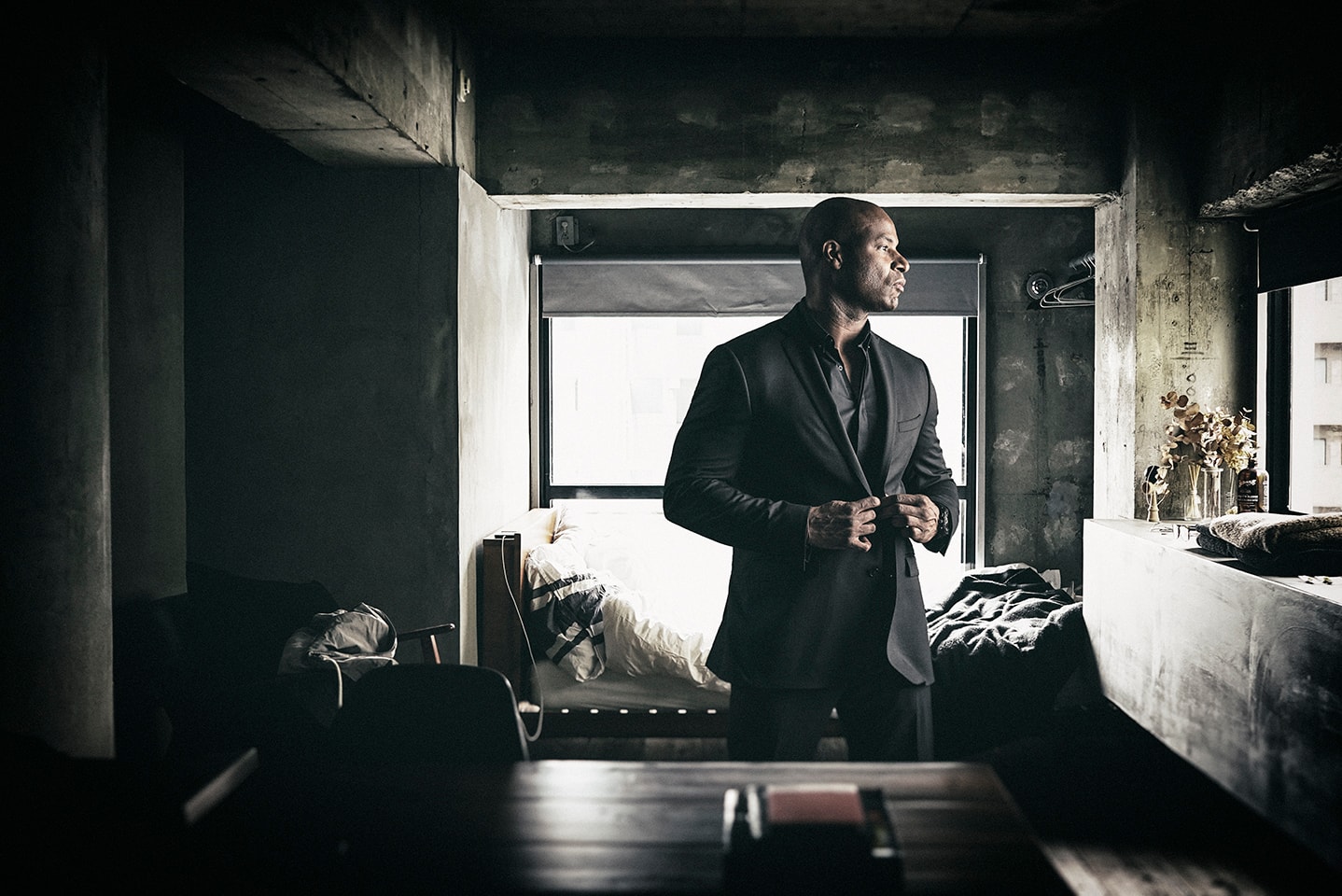 Man in black suit standing by window in moody industrial room