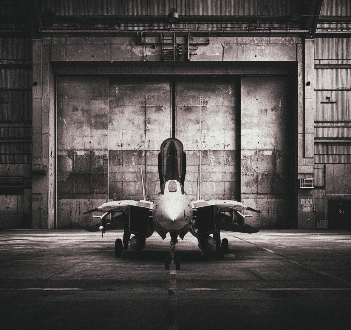 Fighter jet facing forward in a concrete hangar, black and white